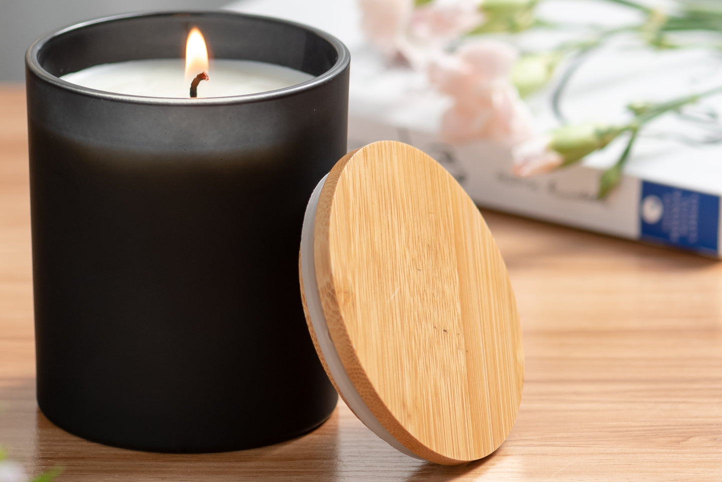 Black candle with wooden lid on a table next to a lamp and book